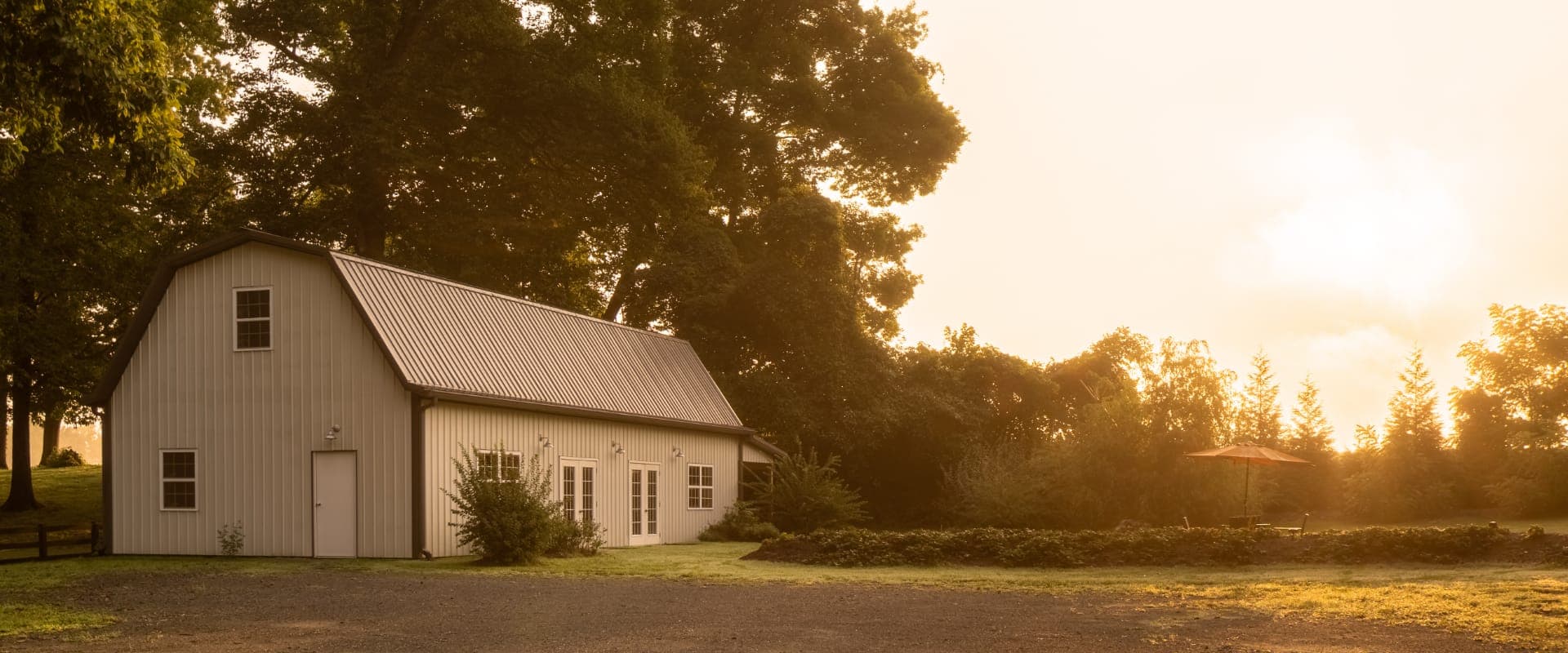 A white barn stands in a lush green landscape during sunrise.