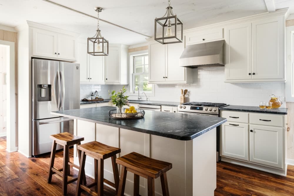 Modern kitchen with white cabinets, black countertop, and wooden stools.