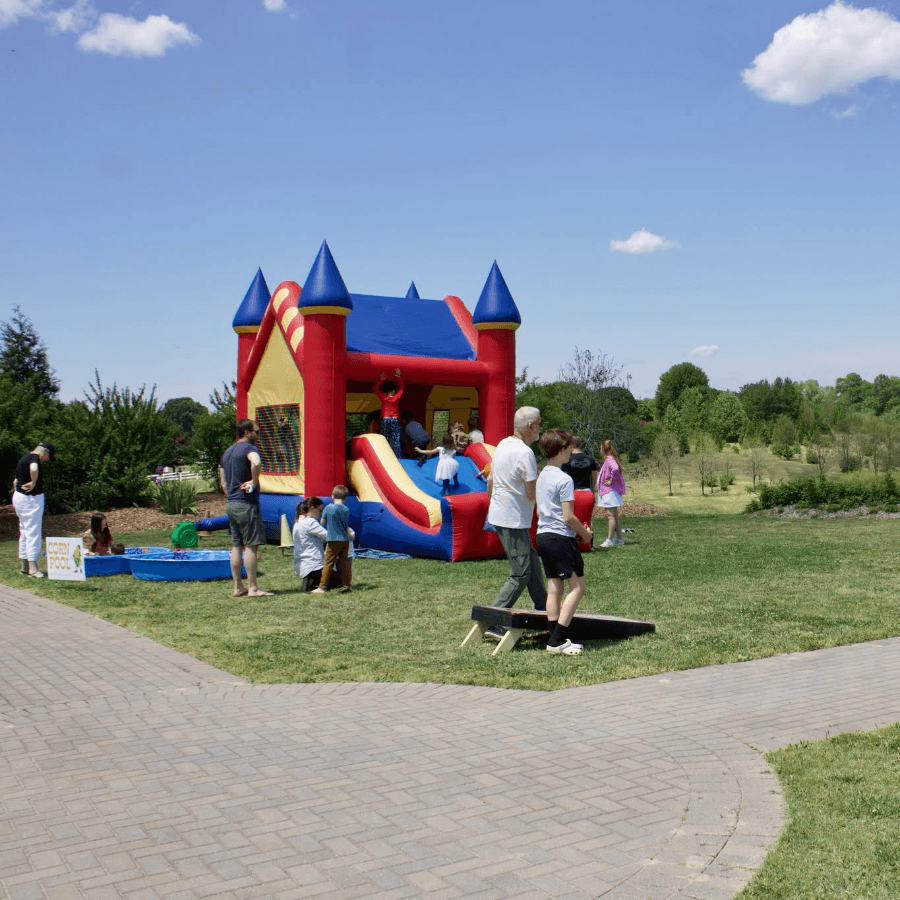A colorful inflatable bounce house is set up in a park, surrounded by children and adults enjoying the sunny day.