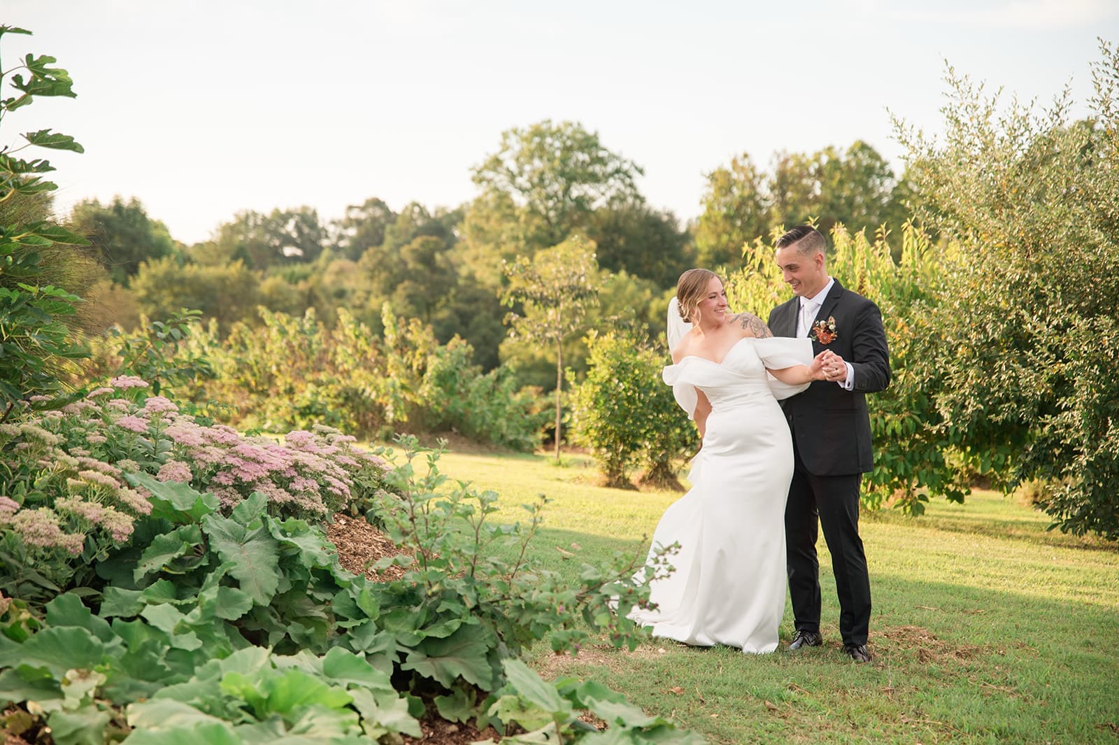 A bride and groom embrace joyfully in a serene outdoor setting filled with greenery and flowers.