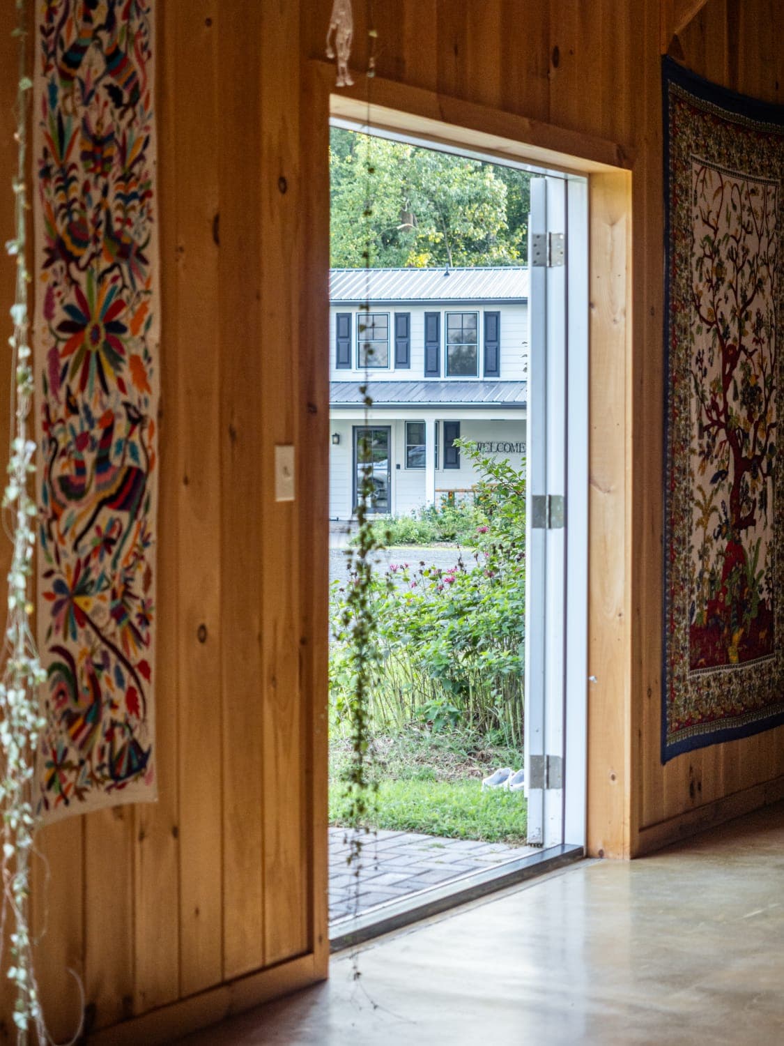 A view from a wooden interior doorway shows a house across the street with lush greenery outside.