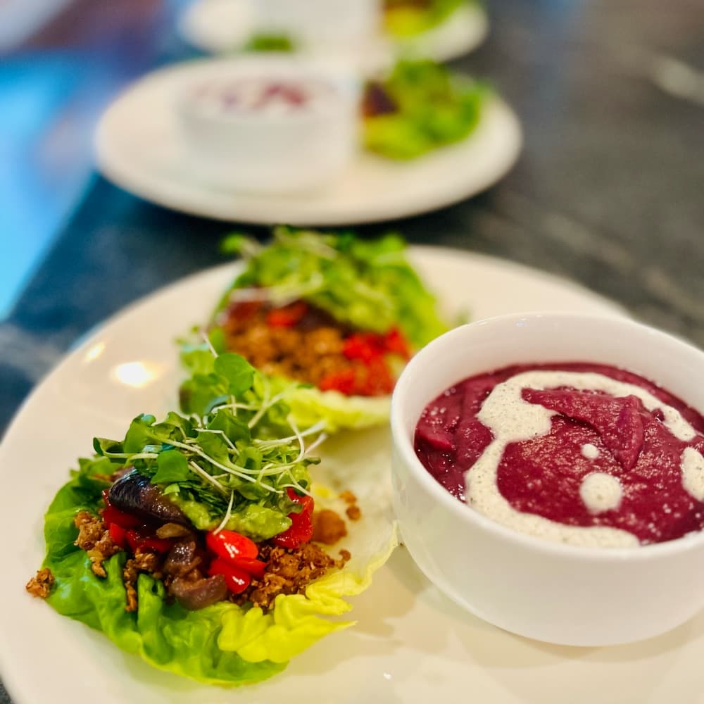 A plate with two lettuce wraps filled with vegetables and a bowl of purple soup garnished with cream.