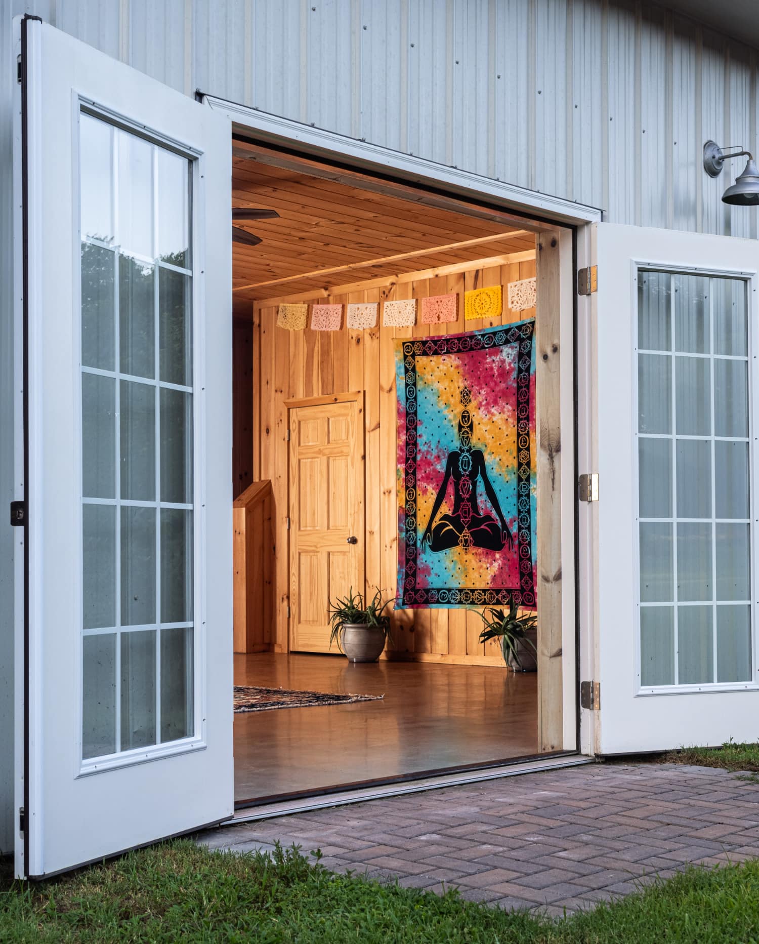View of an open door leading into a cozy, wooden interior decorated with a colorful tapestry and plants.