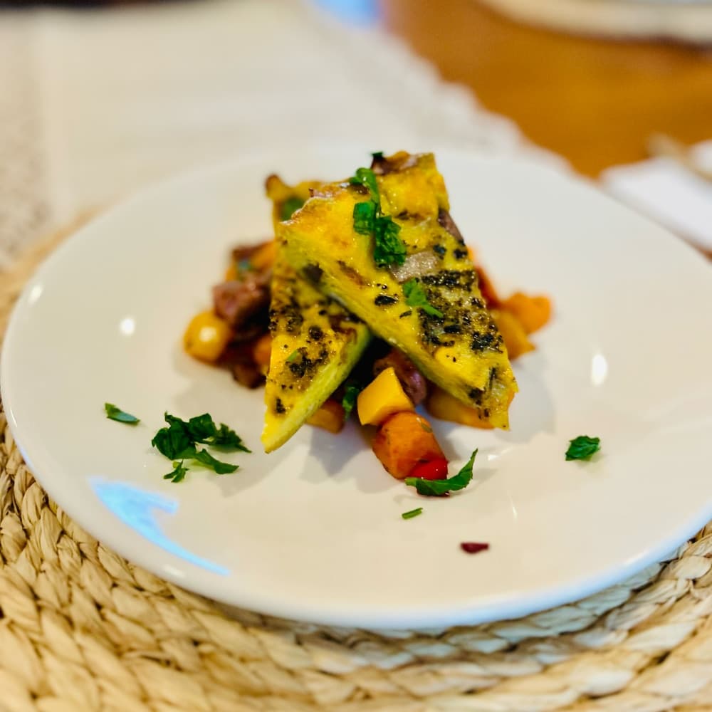 A plate of yellow grilled vegetable wedges topped with herbs, served over a colorful salad.