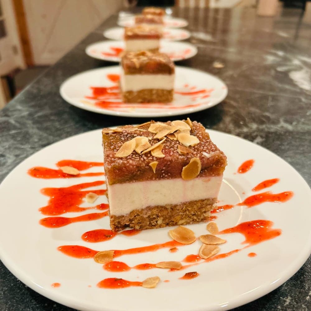 Layered dessert on a white plate with a raspberry sauce and almond flakes.
