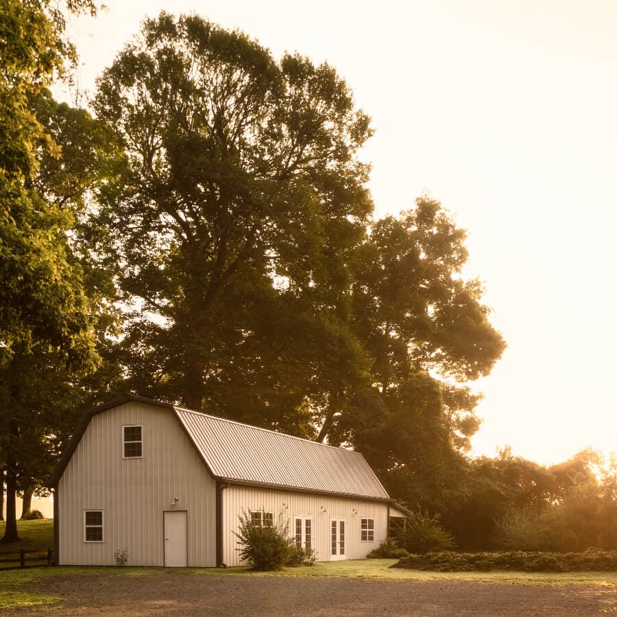 A simple white barn-style building surrounded by trees at sunset.