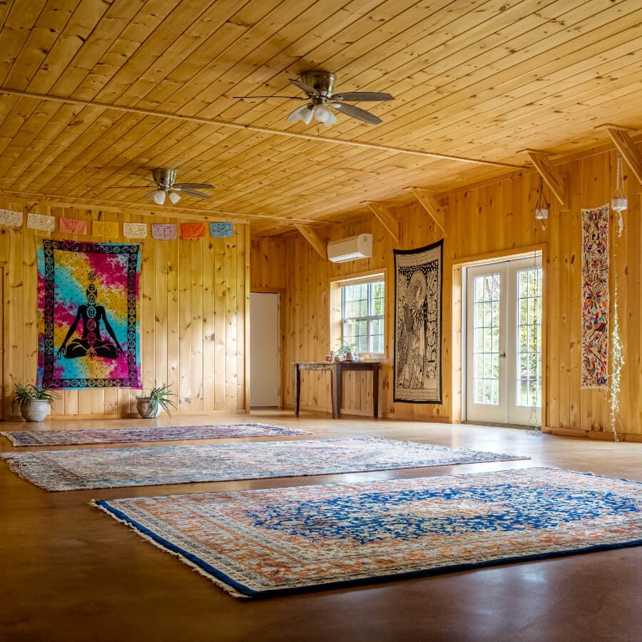 Spacious wooden room with colorful tapestries and area rugs, featuring large windows and a welcoming ambiance.