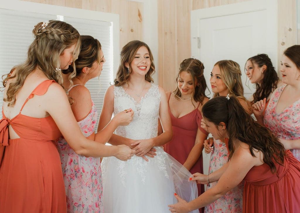 A bride is surrounded by her bridesmaids as they help her dress for the wedding.