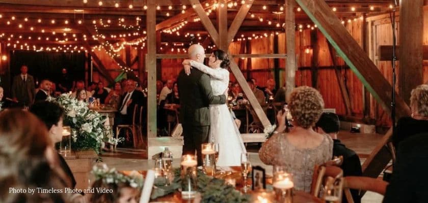 Newlyweds dance inside the rustic barn at Honeys Harvest Farm with warm string lights, dinner tables, and seated wedding guests.