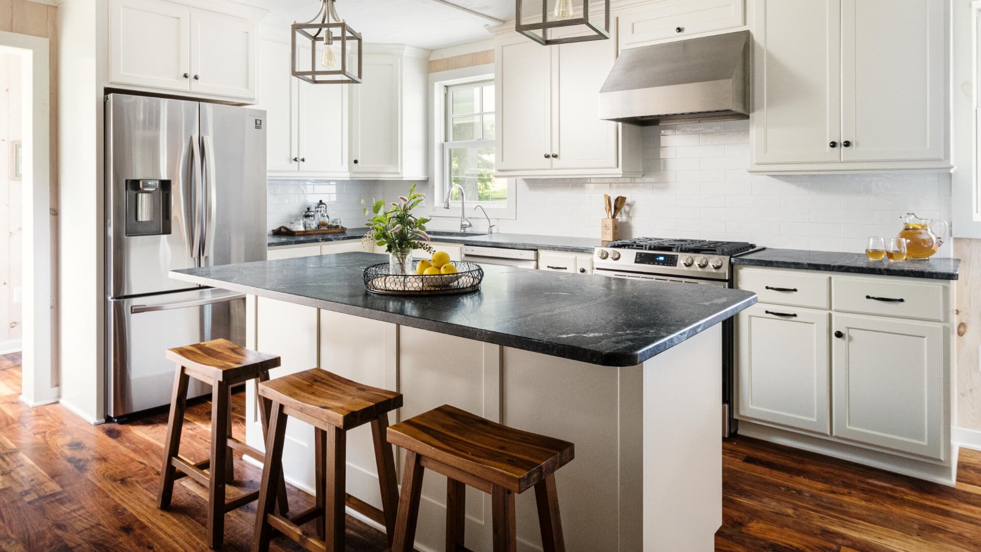 A bright, modern kitchen featuring white cabinets, a dark countertop island, and wooden bar stools.
