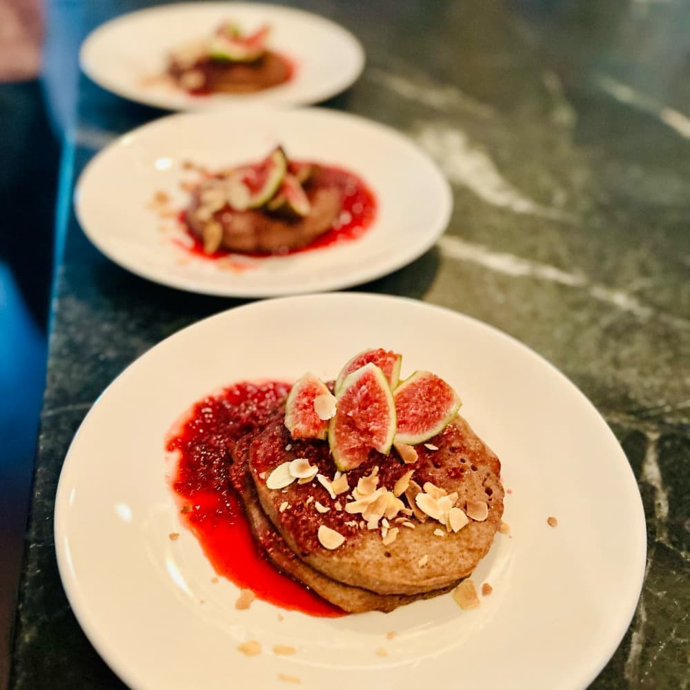 Three plates of pancakes topped with figs, sliced almonds, and raspberry sauce.