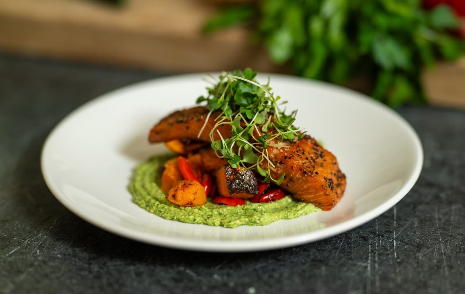 Grilled salmon on a bed of green sauce with colorful vegetables and microgreens.