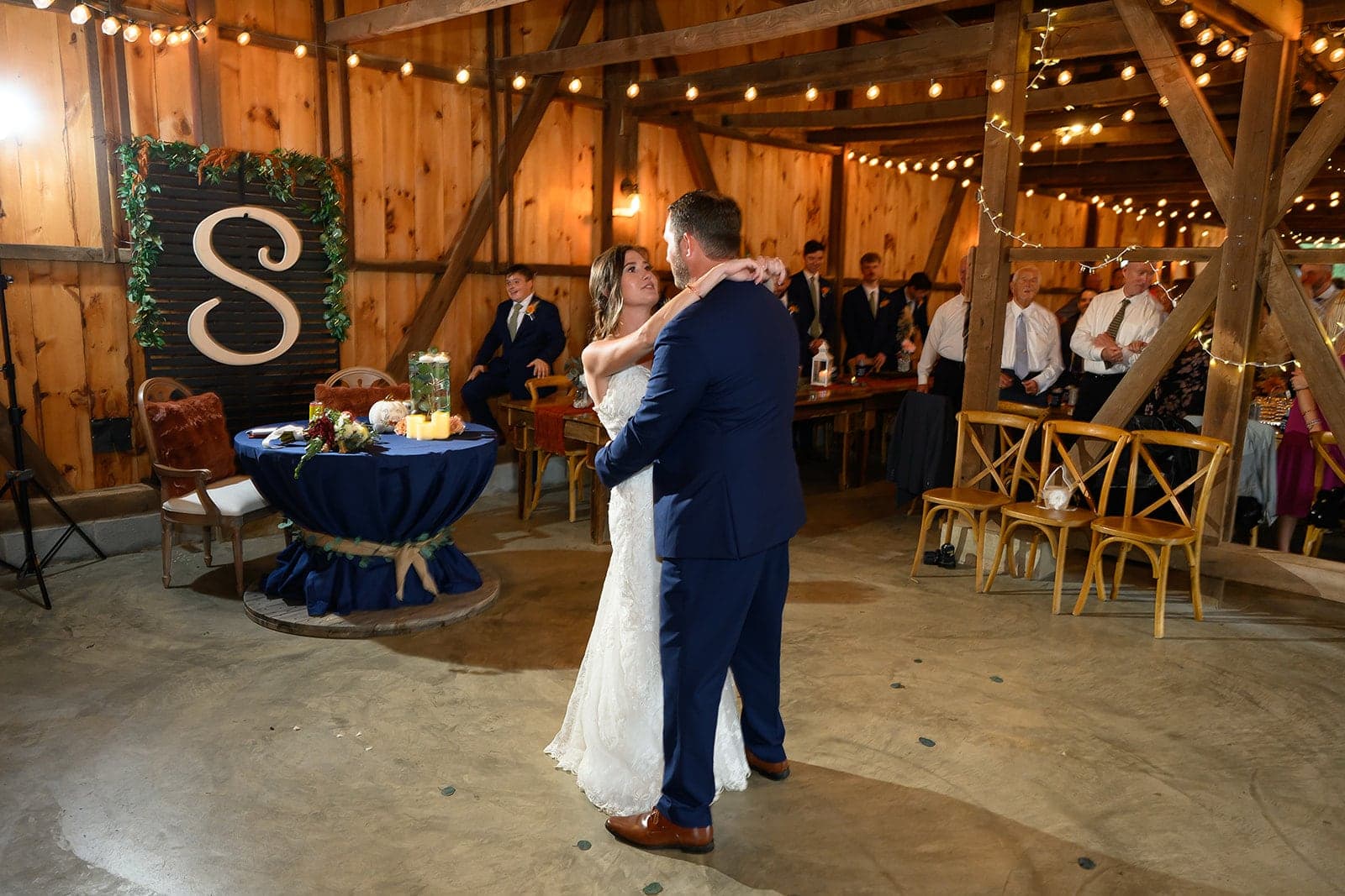 A couple shares their first dance at a rustic wedding reception in a decorated barn.